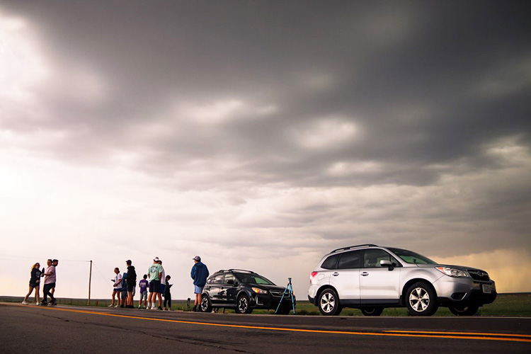 Car and research team sitting under an ominous storm cloud while chasing